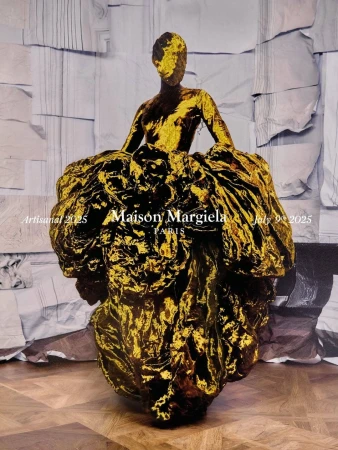 Model wearing a shimmering metallic gold sculptural gown standing against a collaged backdrop in an ad campaign
