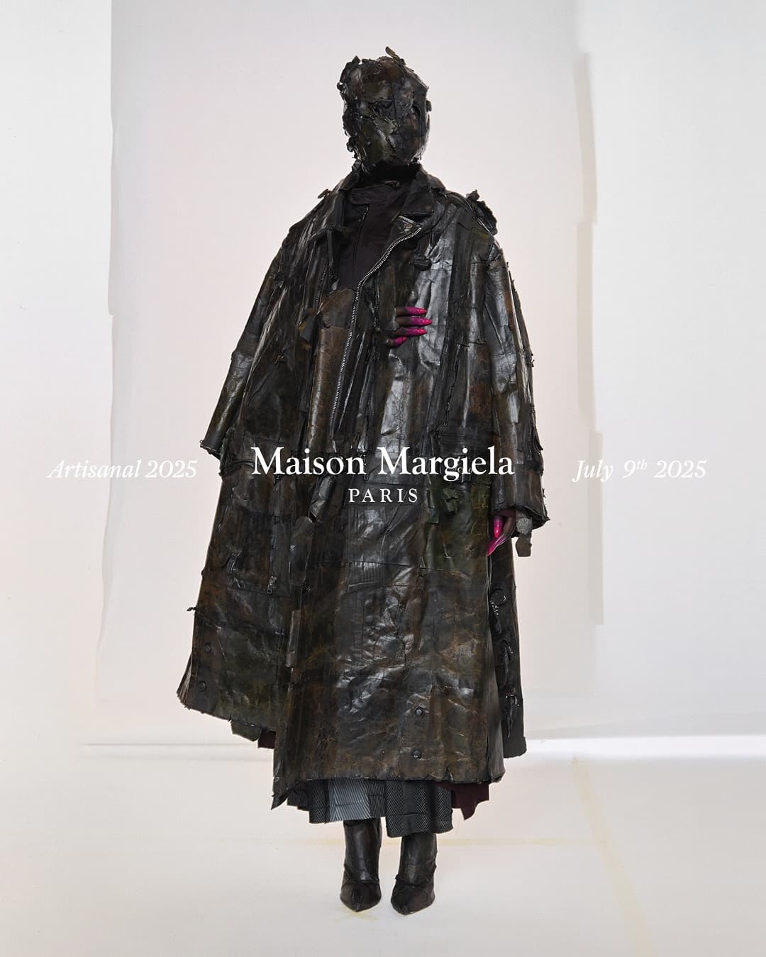 Model wearing dark textured leather coat and matching headpiece against white backdrop with Maison Margiela typography