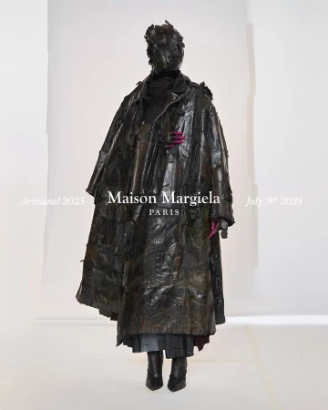 Model wearing dark textured leather coat and matching headpiece against white backdrop with Maison Margiela typography