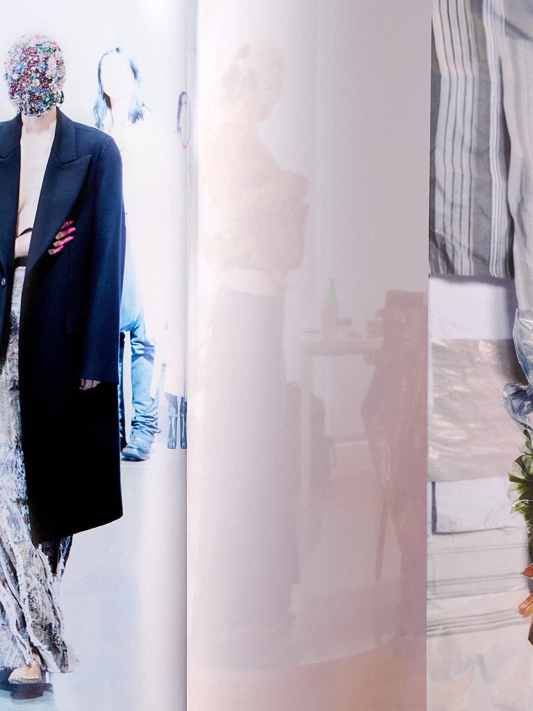 Model in dark coat with embellished face mask standing against bright backdrop for Maison Margiela Artisanal campaign.
