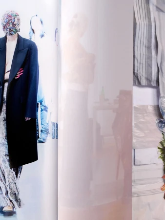 Model in dark coat with embellished face mask standing against bright backdrop for Maison Margiela Artisanal campaign.