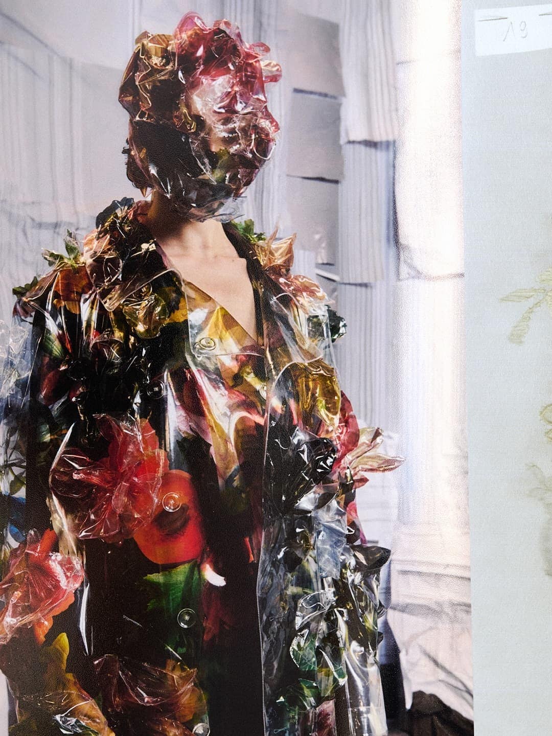Model wearing a translucent floral-patterned vinyl coat and matching headpiece by Maison Margiela.