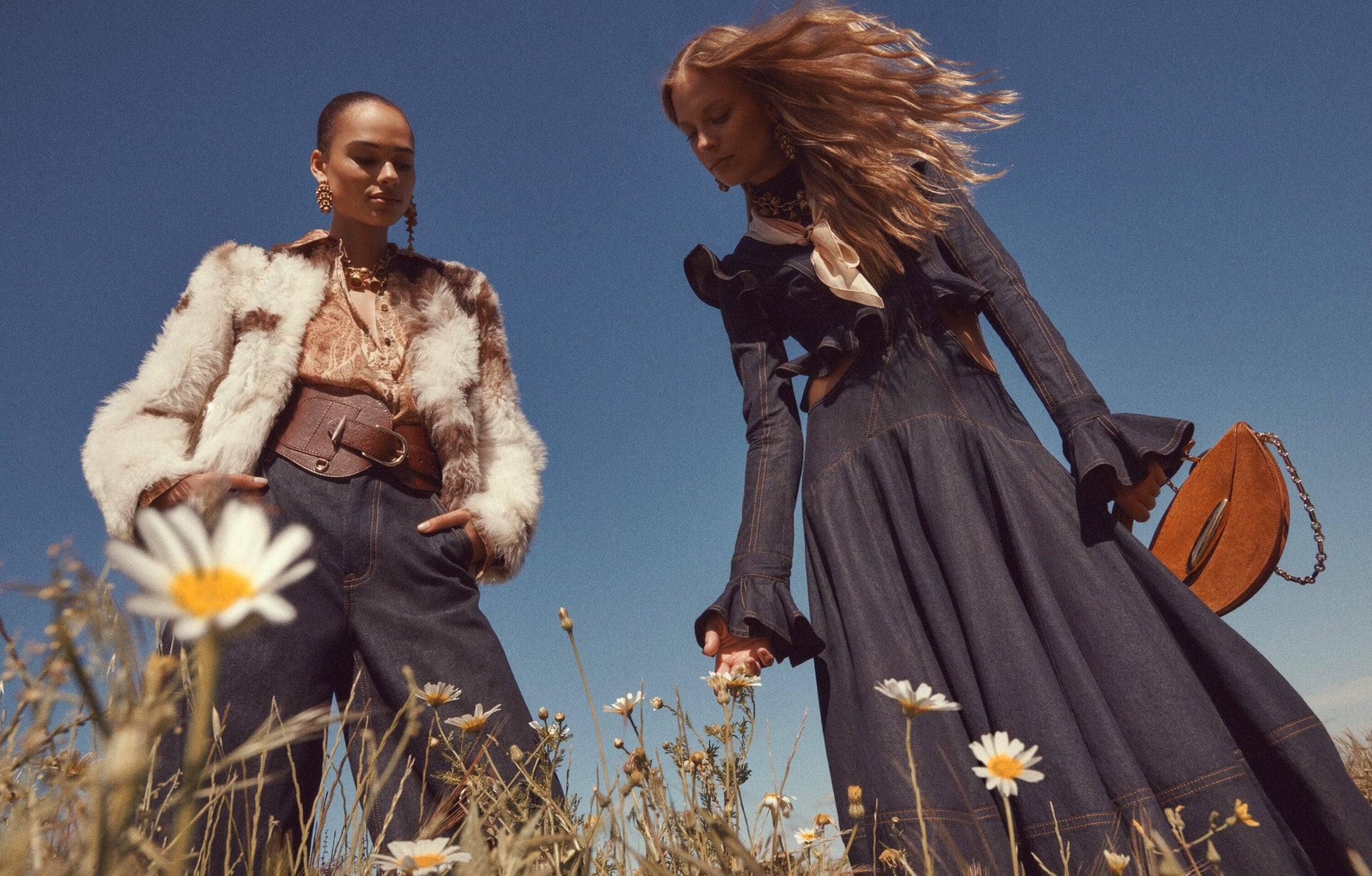 Two female models in denim and patterned apparel posing in a sunny wildflower field for Zimmermann Fall 2025 ad campaign.