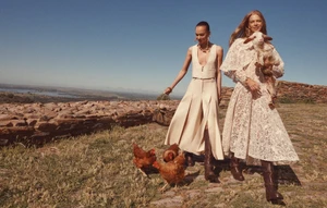 Two female models posing outdoors on a sunny hill with chickens and a lamb, photographed by Benny Horne for Zimmermann.