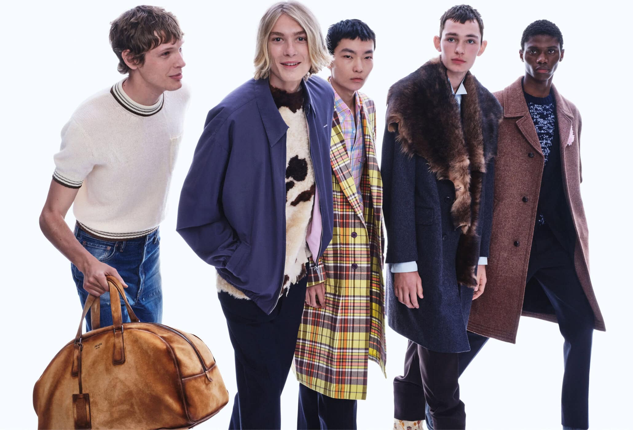 Group of five male models wearing layered winter coats and knitwear against a bright white background for Prada ad campaign.