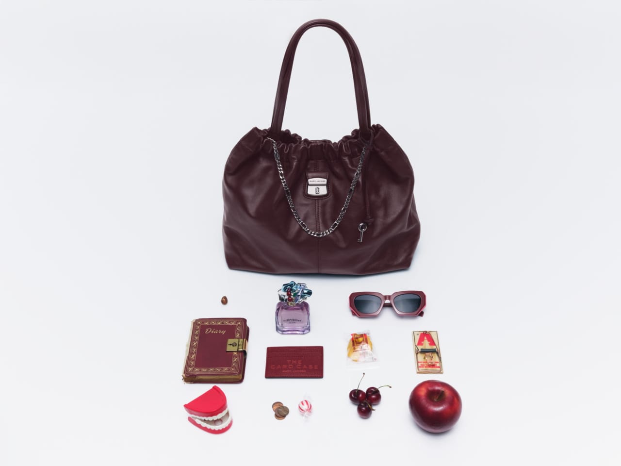 Burgundy leather handbag displayed above a collection of small accessories and objects against a white background.