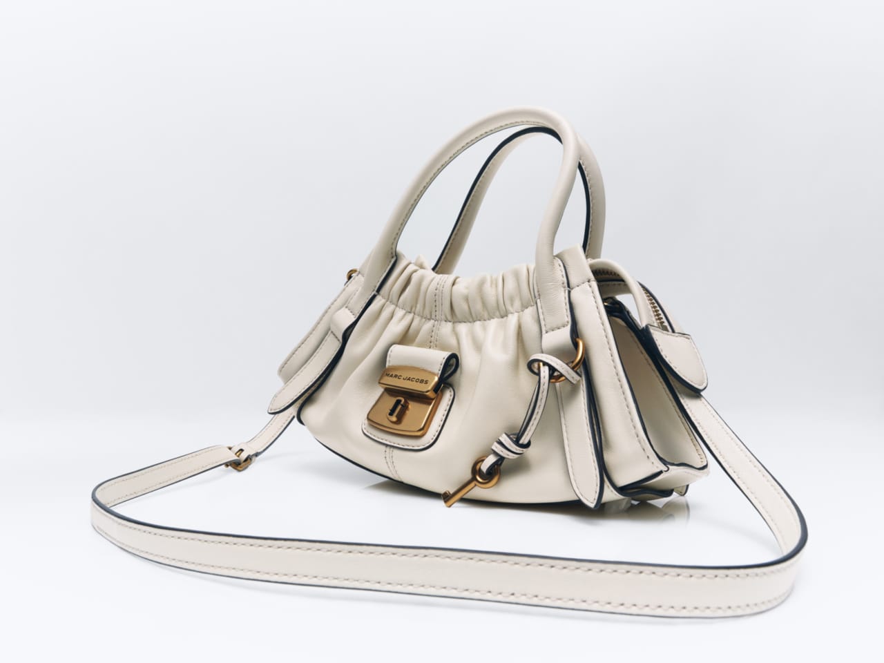 Off-white leather Marc Jacobs handbag with gold hardware and shoulder strap on white background