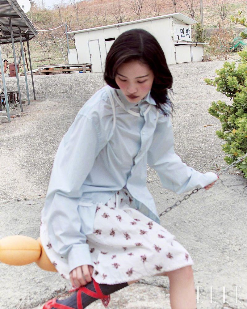 A young woman in a casual outfit is sitting on a yellow swing in an outdoor setting. The photo captures a relaxed, lifestyle moment.
