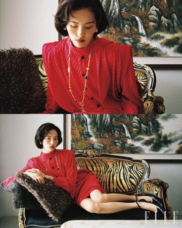 A woman in a red dress poses on a patterned couch near a nature painting, highlighted by classic fashion and elegant decor.