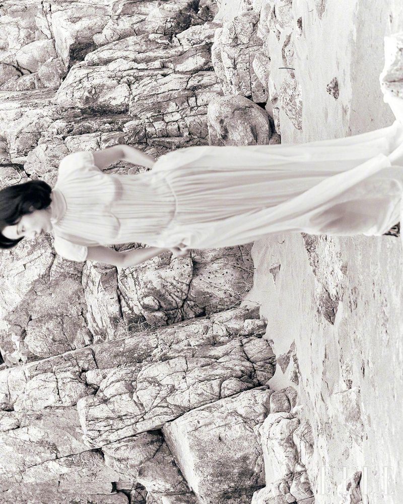 Monochrome portrait of a woman in a dress posing against a rocky cliff face, creating a blend of fashion and nature.
