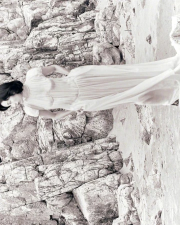Monochrome portrait of a woman in a dress posing against a rocky cliff face, creating a blend of fashion and nature. 