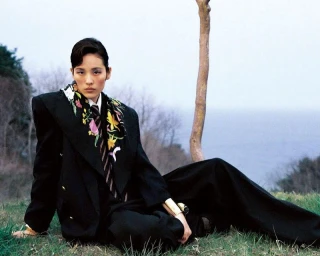 Model seated on grassy ground wearing dark oversized blazer and patterned floral scarf for Elle Korea editorial