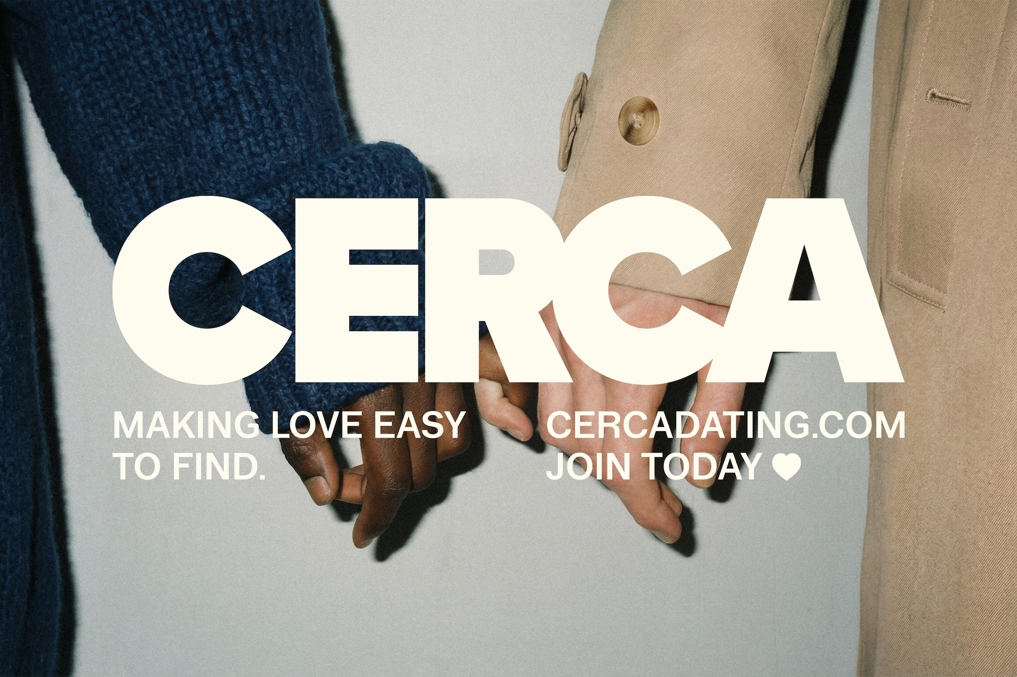 Two people holding hands against a grey wall, wearing a blue knit sweater and a beige coat, for brand CERCA.