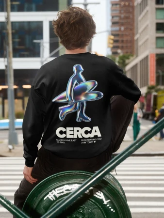 Man from behind wearing a black sweatshirt with a chrome graphic illustration and the text CERCA against an urban street background.
