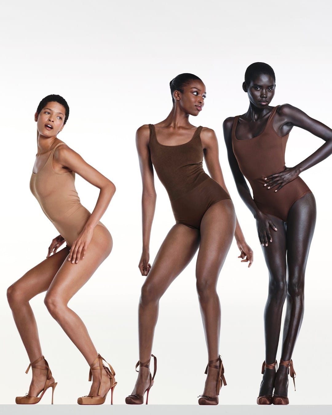 Three models wearing swimsuits and lace-up high heels posing against a white seamless background for Christian Louboutin
