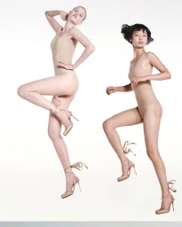 Two models wearing nude bodysuits and lace-up high heels posing dynamically against a clean white seamless background.