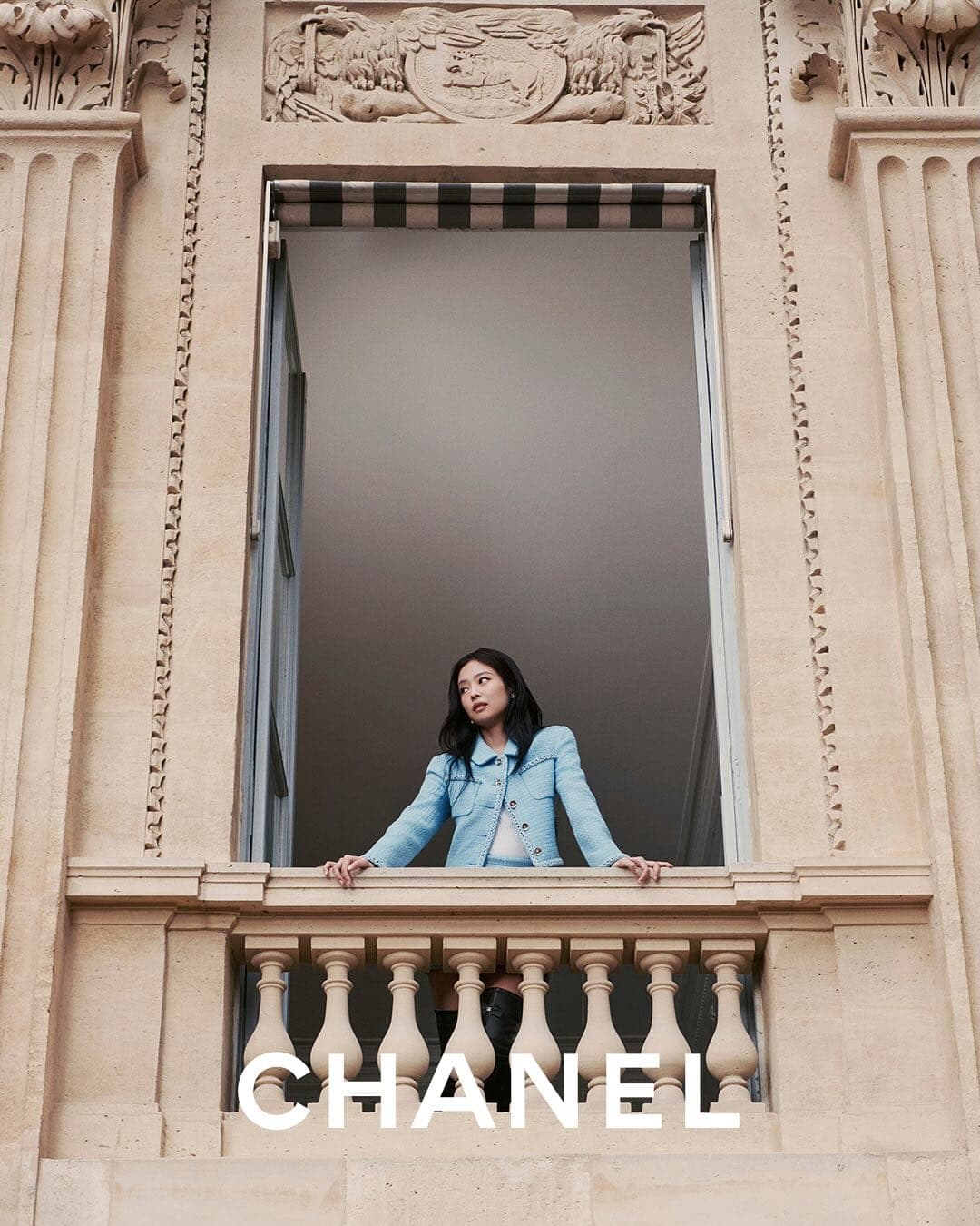 Jennie wearing a light blue tweed jacket leaning on a stone balcony railing at Palais-Royal in Paris for Chanel