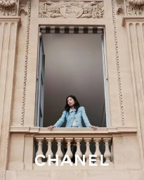 Jennie wearing a light blue tweed jacket leaning on a stone balcony railing at Palais-Royal in Paris for Chanel