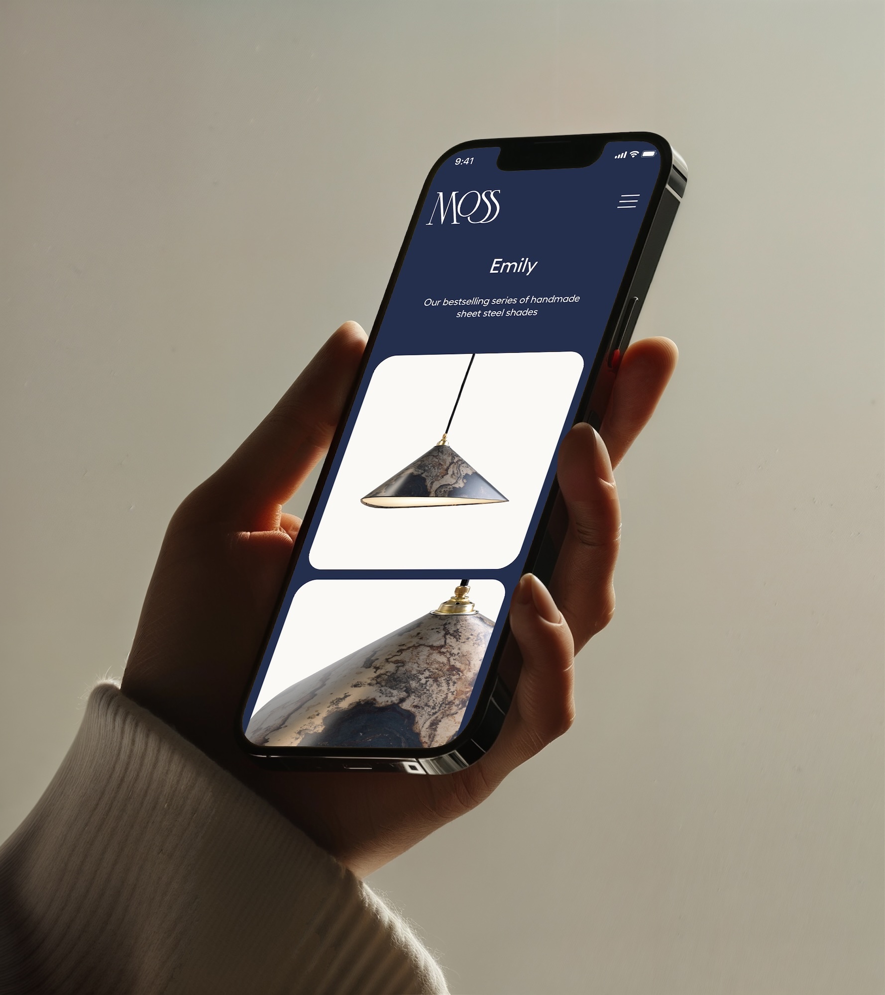 Hand holding a smartphone displaying the MOSS Objects brand website with product images of steel lamp shades.