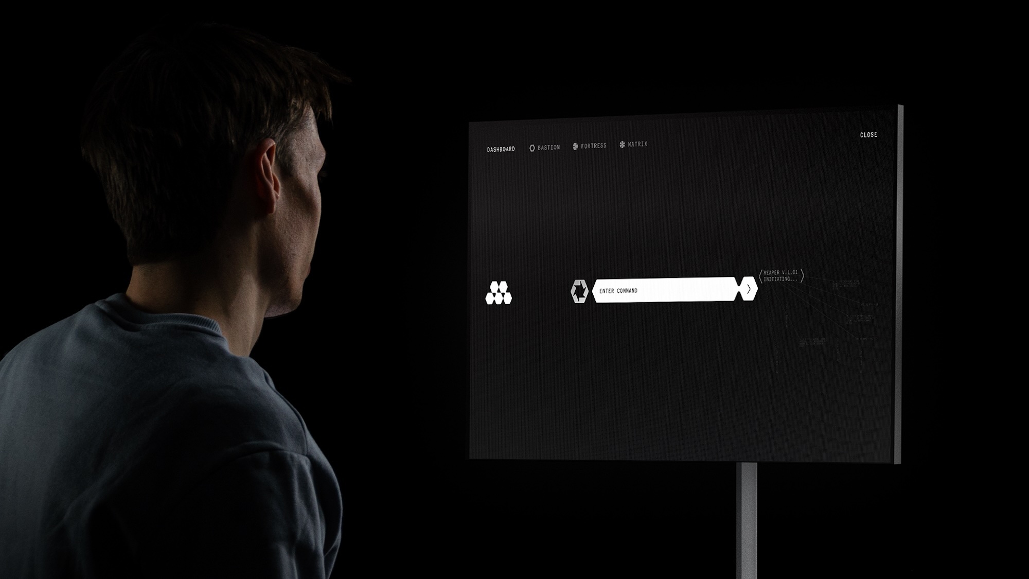 A man in profile wearing a blue sweater facing a digital display screen showing a dark interface with white text against a black background.