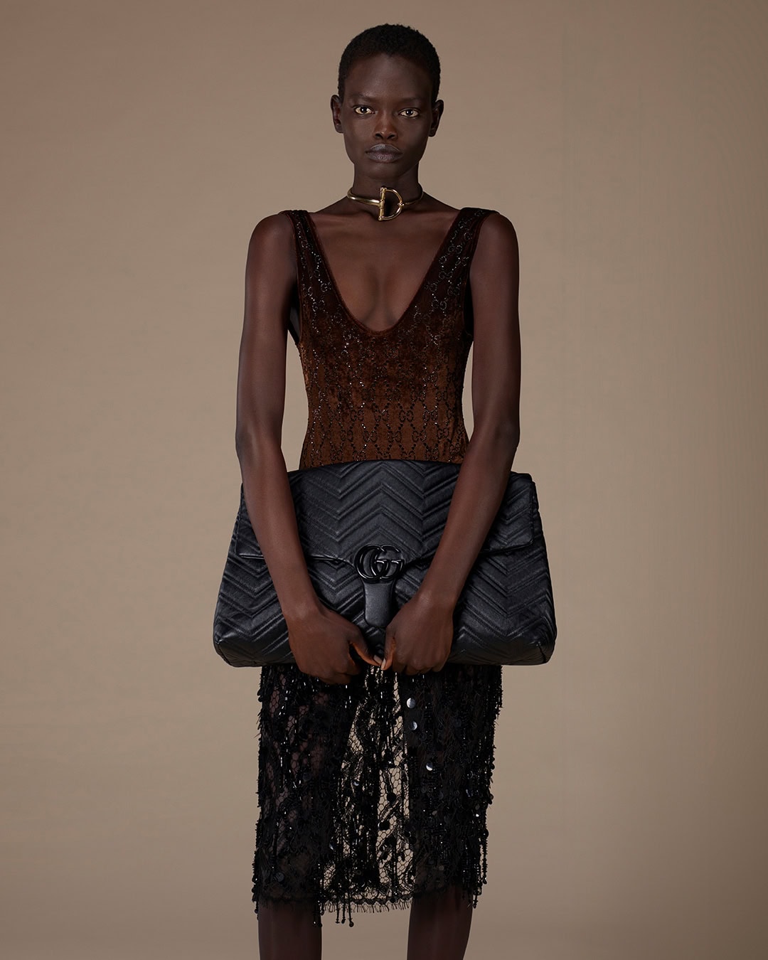 Model wearing a dark sequined sleeveless top and black quilted handbag against a neutral studio background
