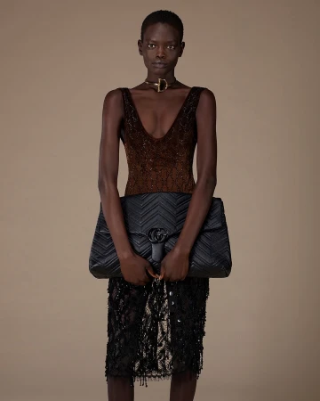 Model wearing a dark sequined sleeveless top and black quilted handbag against a neutral studio background