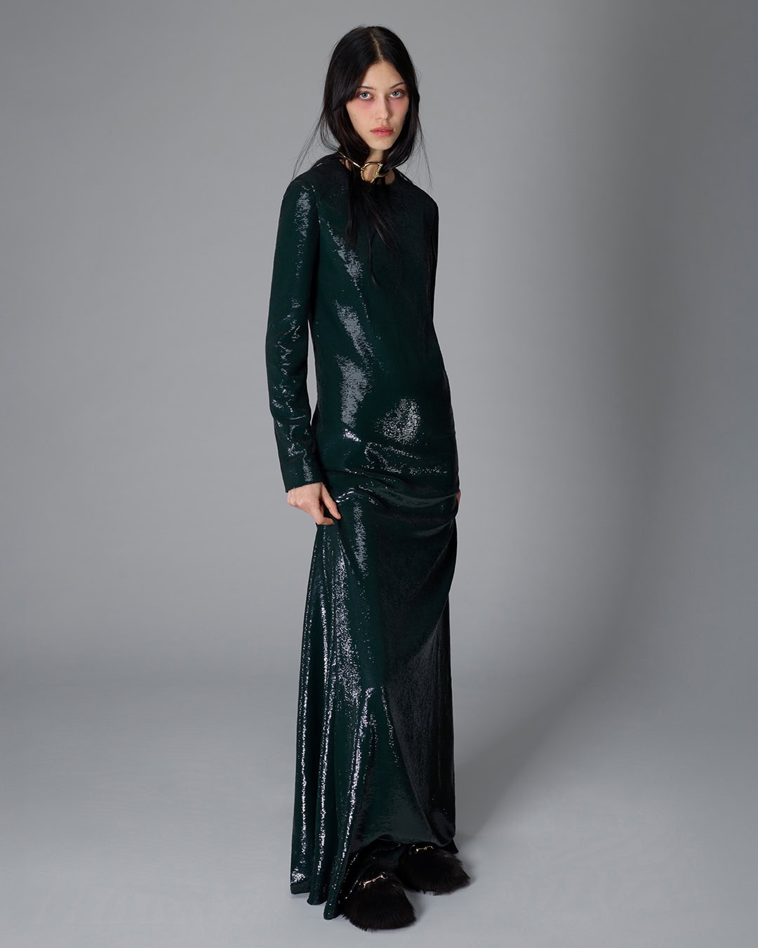 Model wearing a dark green sequin long sleeve dress against a neutral grey studio seamless background.
