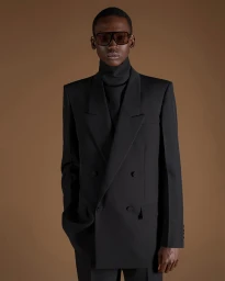 Model wearing a structured black double-breasted blazer and turtleneck against a warm brown backdrop for Gucci.