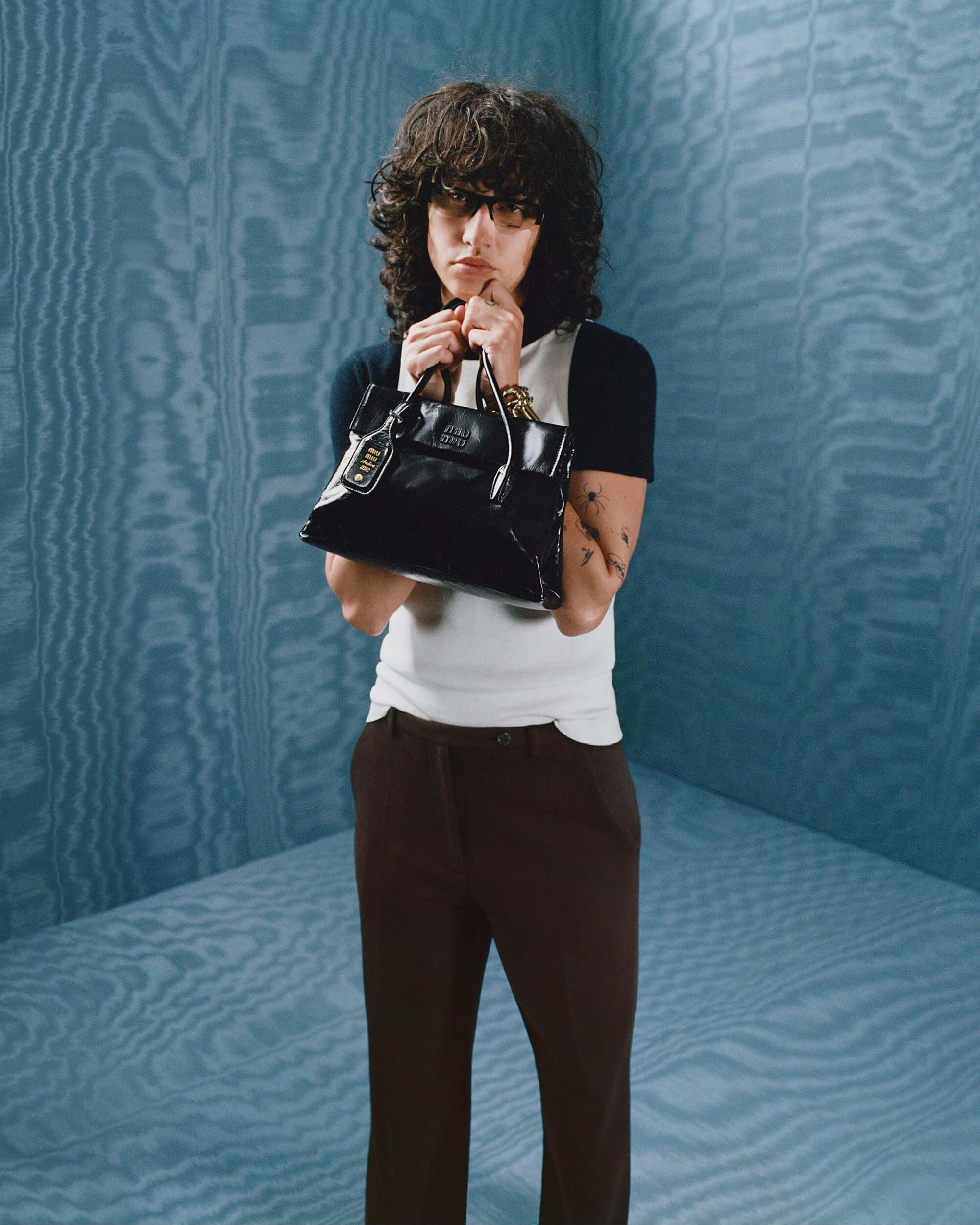 Model holding a black handbag against a textured blue backdrop for Miu Miu Fall 2025 campaign