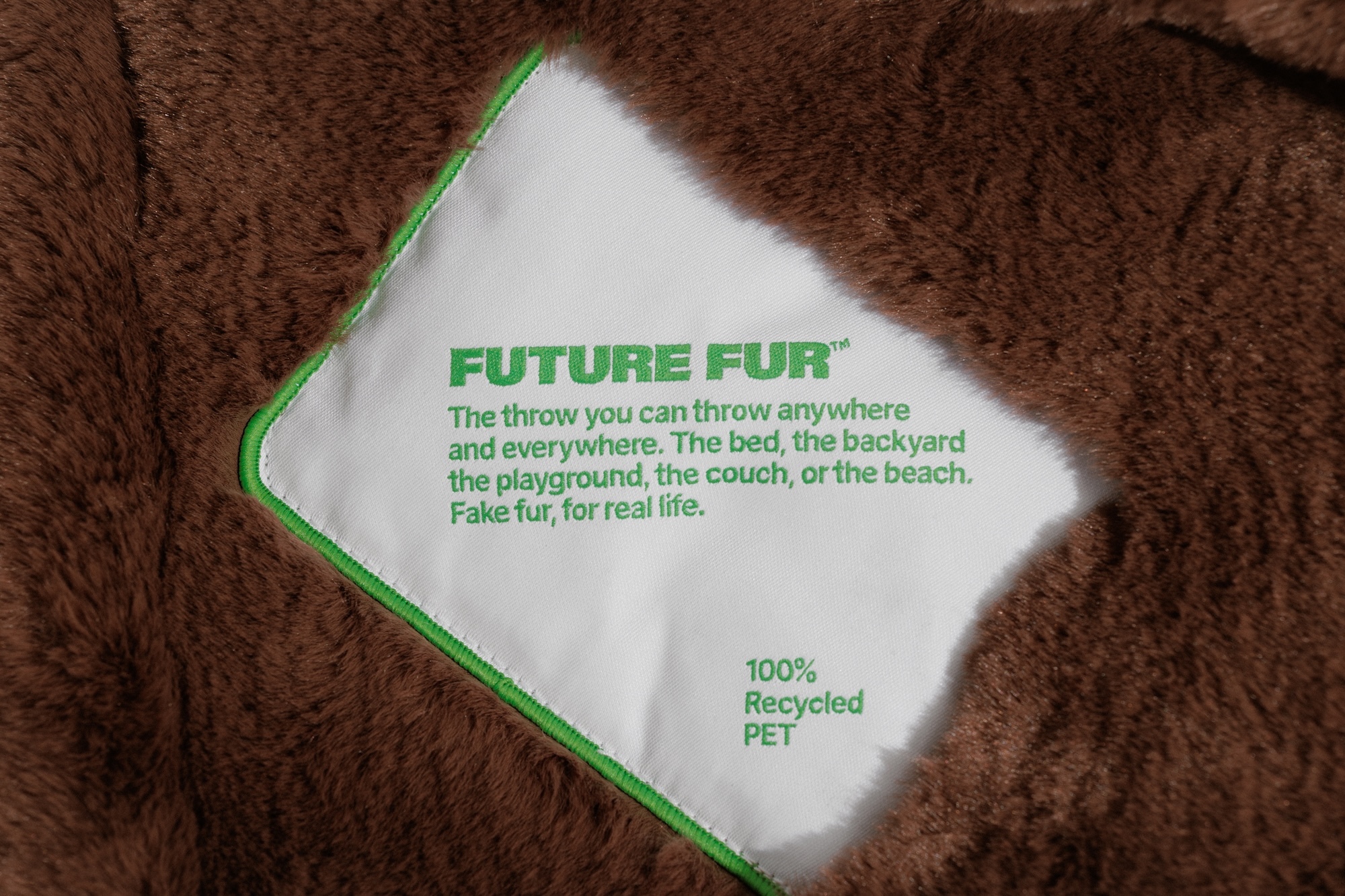 Close-up of a white product label with green text stitched onto textured brown faux fur fabric.