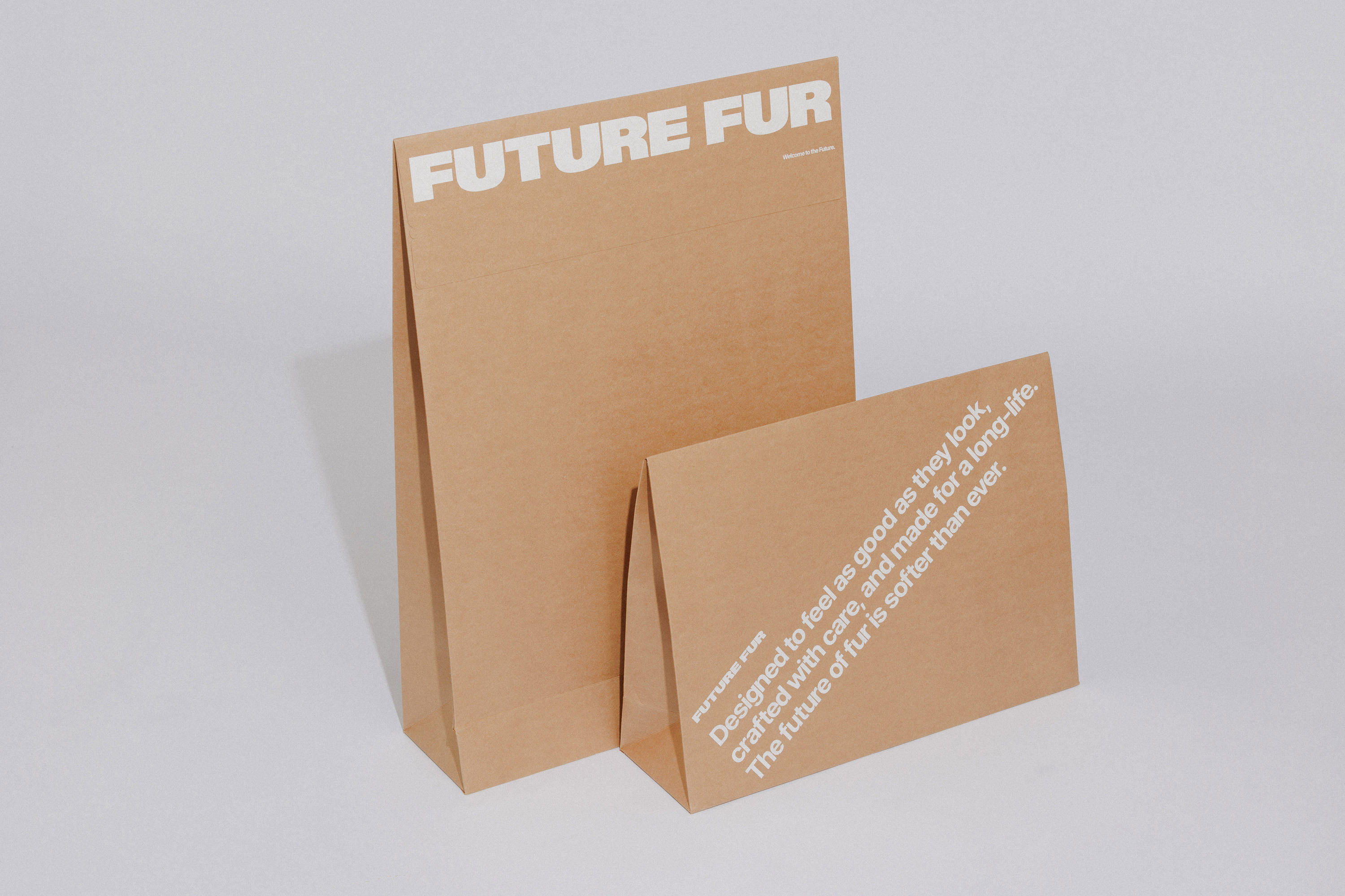 Two brown paper bags with white typography branding set against a clean white seamless studio background.