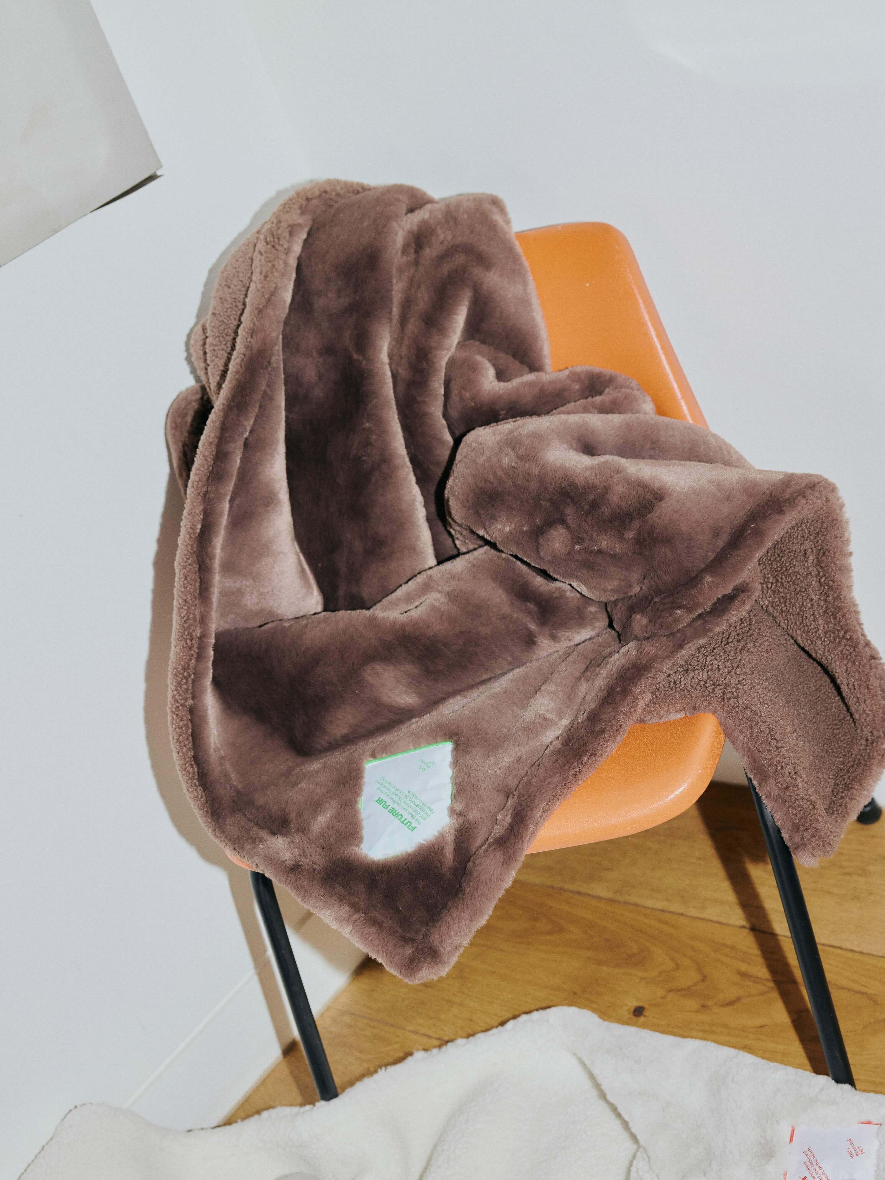Brown faux fur fabric draped over an orange chair against a white wall with wooden flooring