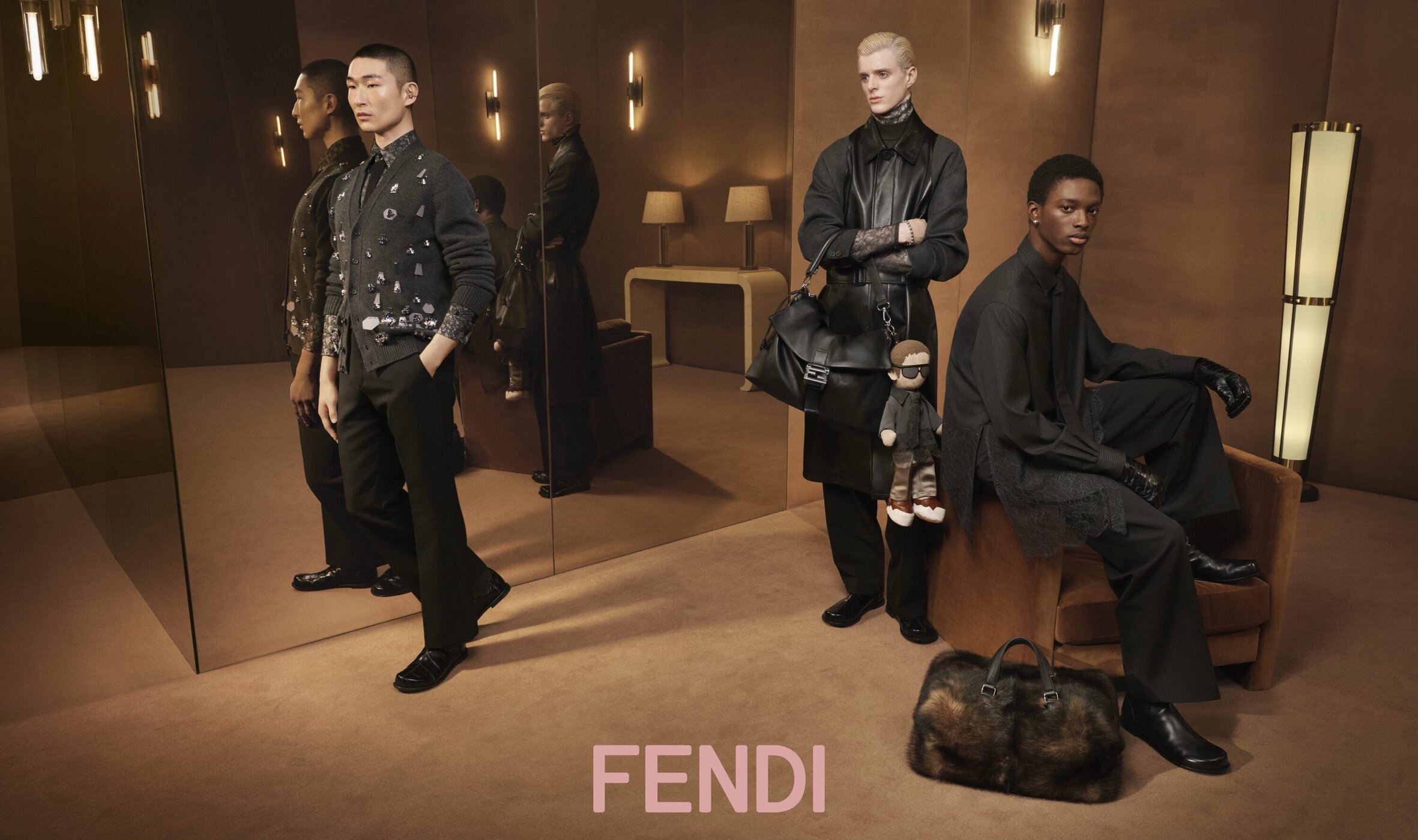 Three models wearing dark menswear apparel inside an interior room with large mirrors and warm lighting for a Fendi campaign