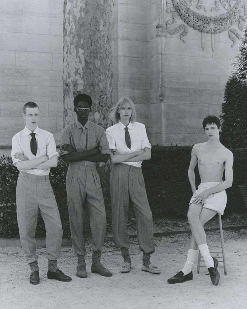 Four young adults in coordinated formalwear pose outdoors in a formal garden in a black-and-white fashion editorial setting.