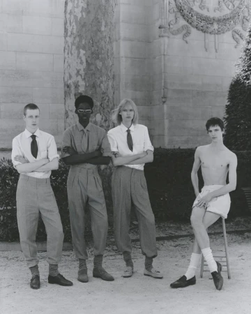 Four young adults in coordinated formalwear pose outdoors in a formal garden in a black-and-white fashion editorial setting.