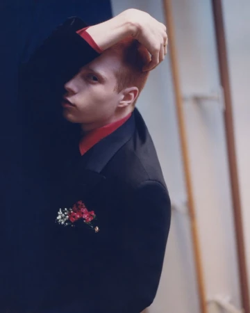 Portrait of red-haired male in dark suit with floral detail against two-tone backdrop in a studio with soft lighting and shallow depth of field.