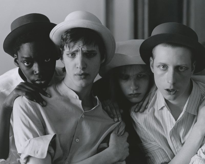 Group of four androgynous people in hats and shirts, staring at the camera, black and white photography, portrait, indoor setting.