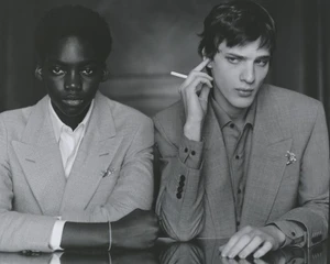 Black and white portrait of two models wearing tailored blazers, seated at a reflective table for a Loro Piana editorial.