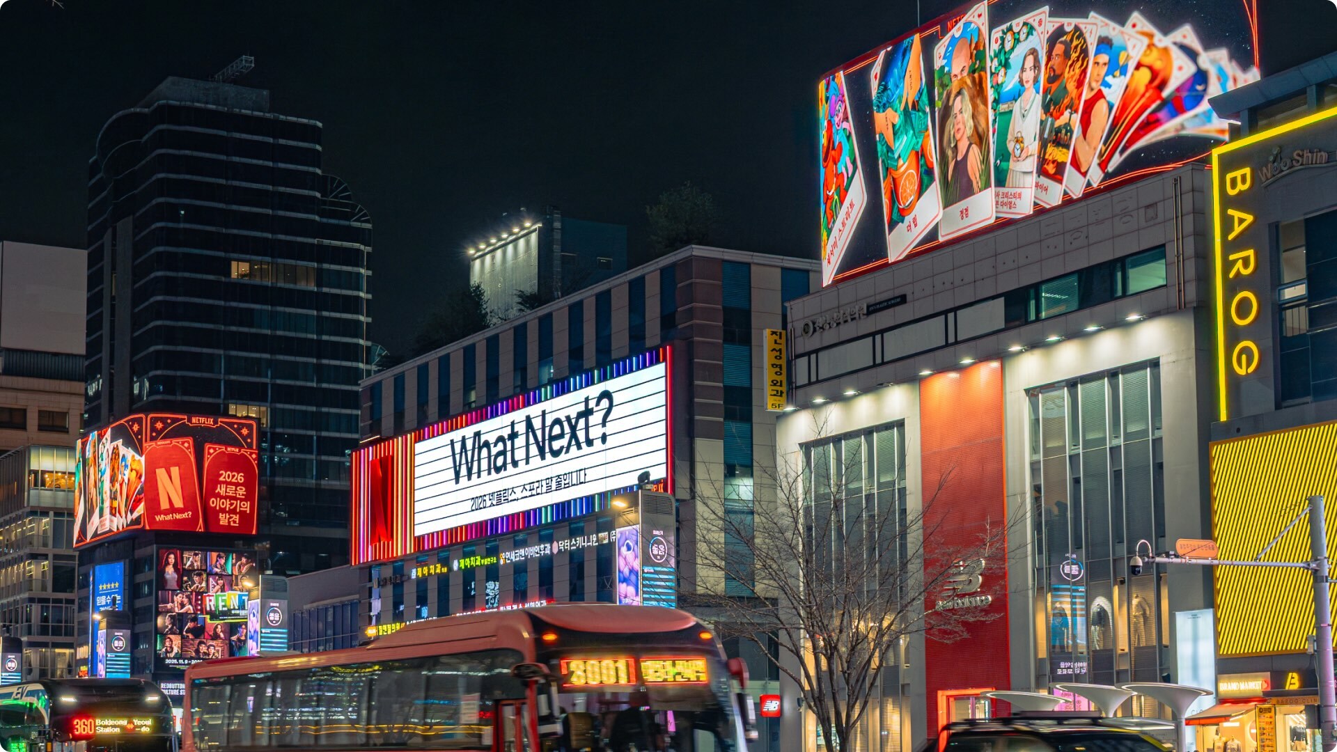Night city street scene featuring large illuminated digital billboards displaying promotional graphics and text for Netflix against urban architecture.