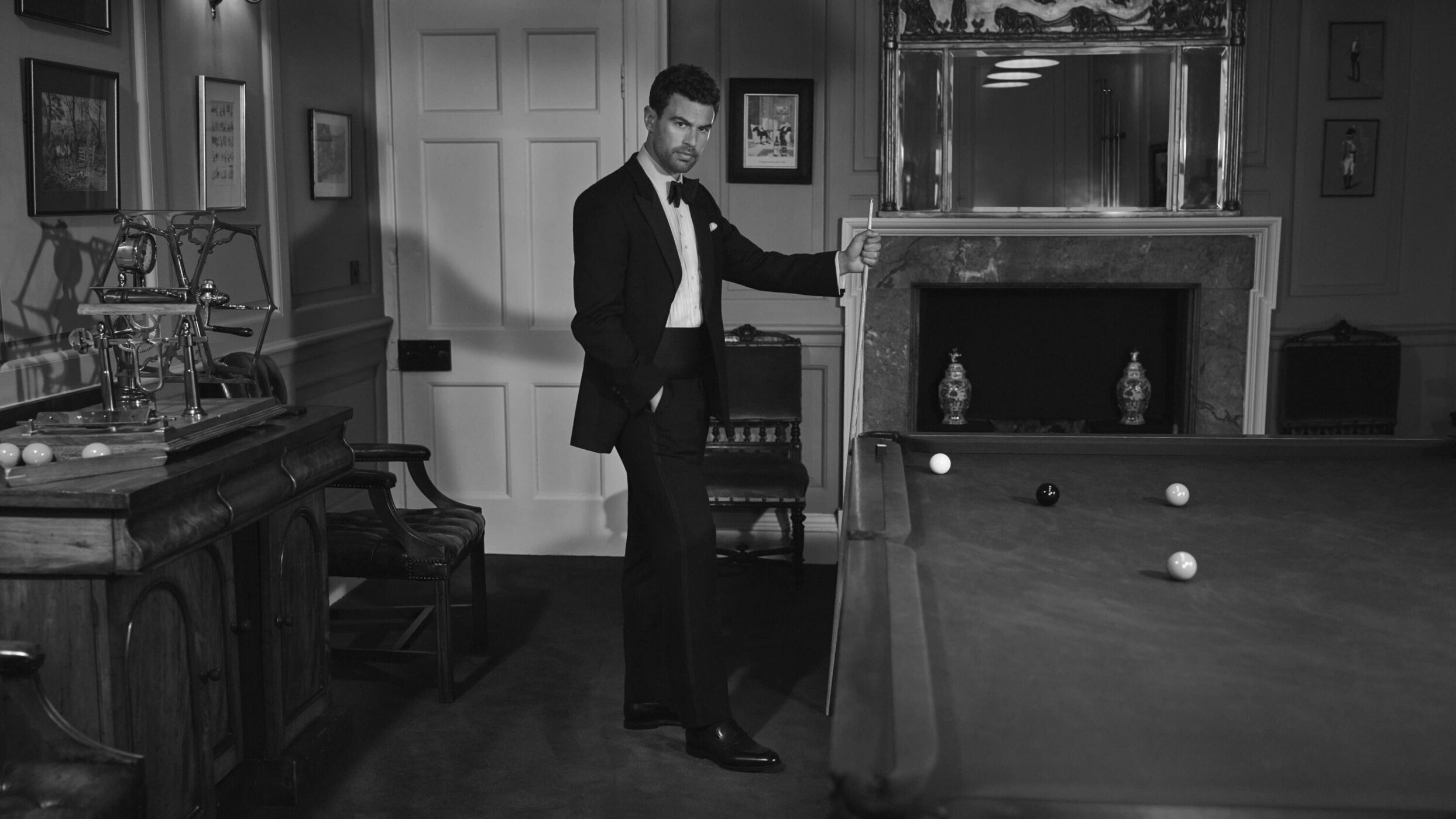 Man in a tuxedo standing by a billiard table inside a wood-paneled room