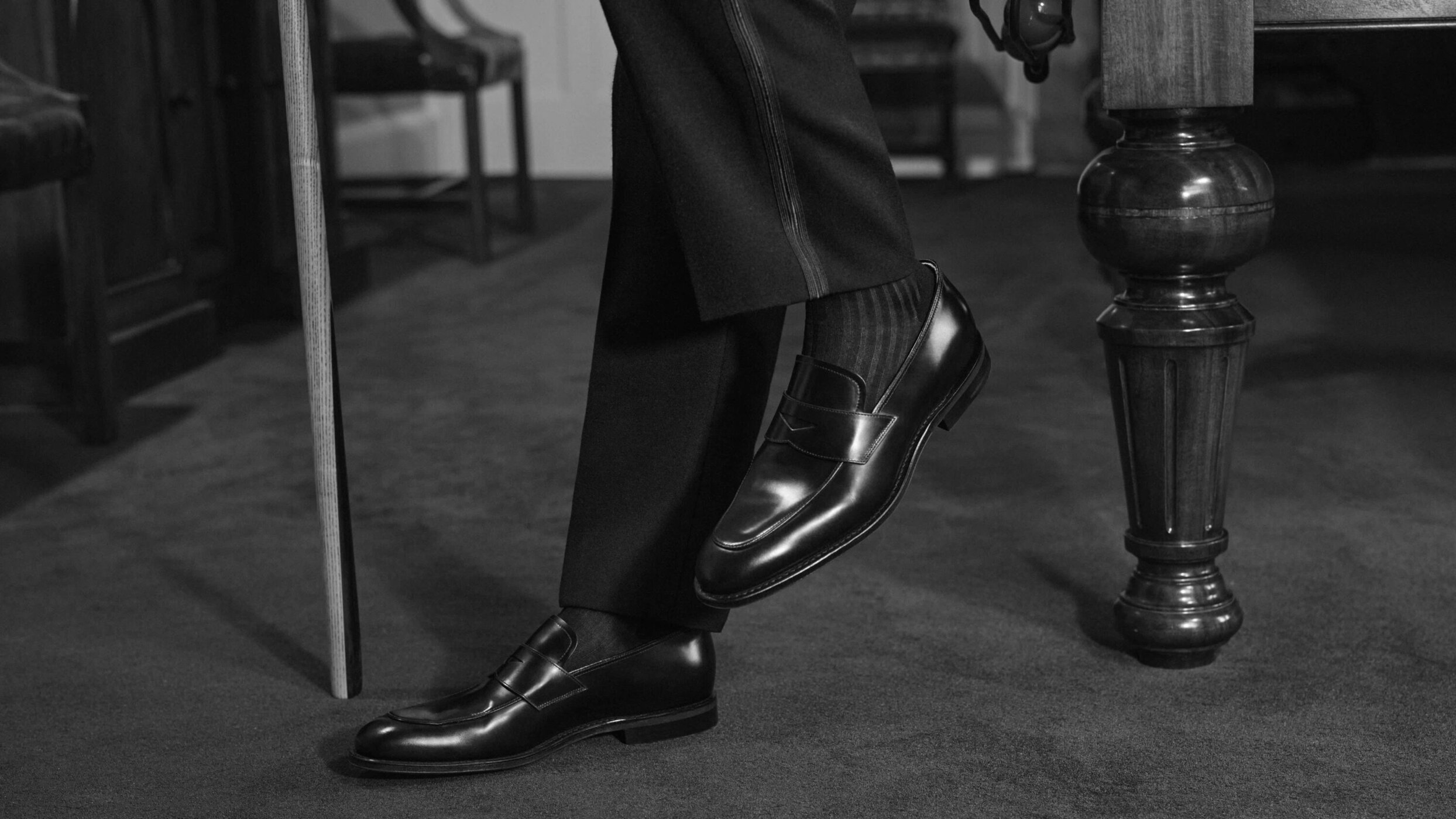Close-up of polished black leather loafers on a person wearing dark trousers and ribbed socks standing on carpet