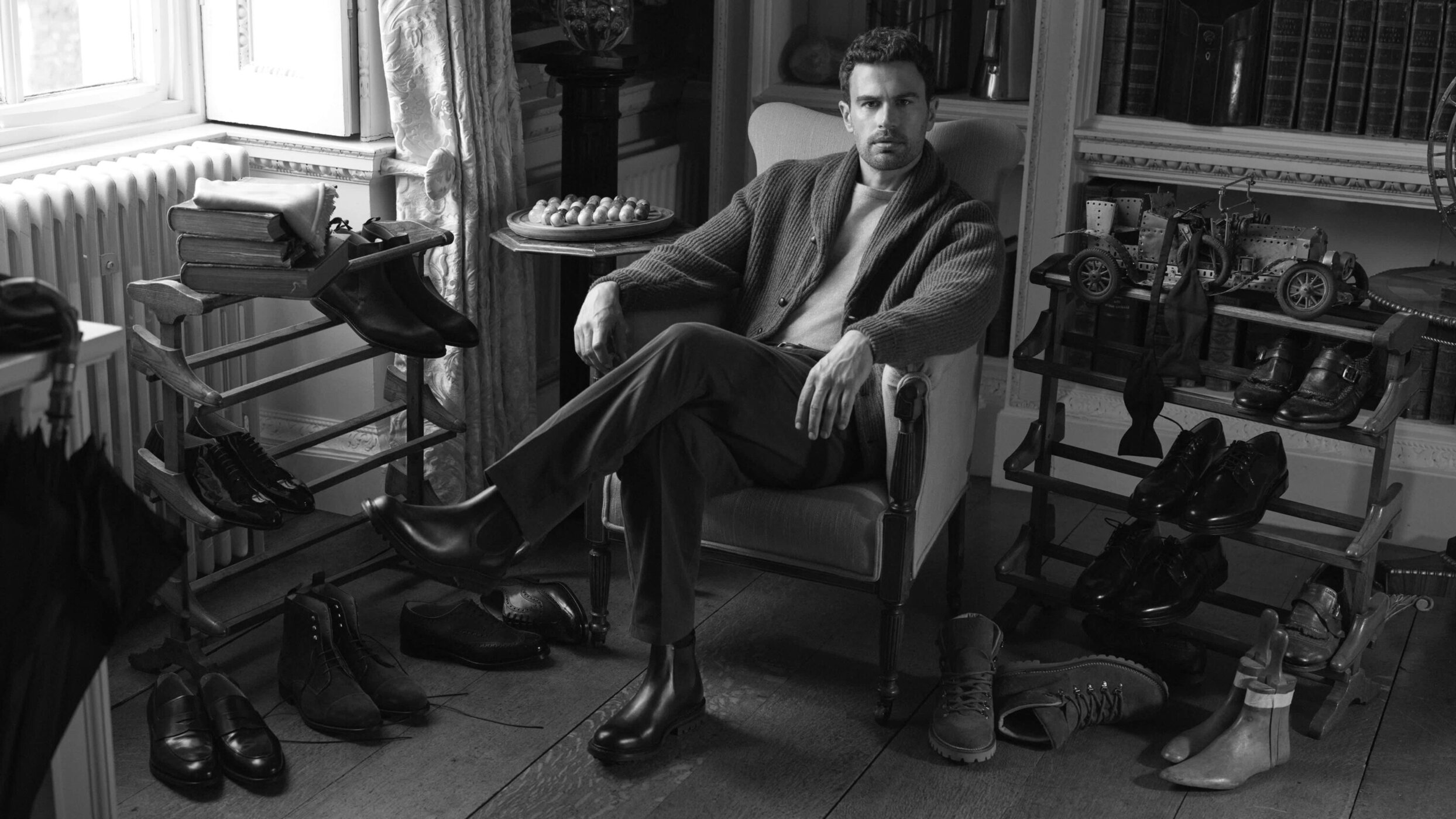 Theo James seated in an armchair surrounded by multiple pairs of leather shoes for Church's Fall 2025 campaign.