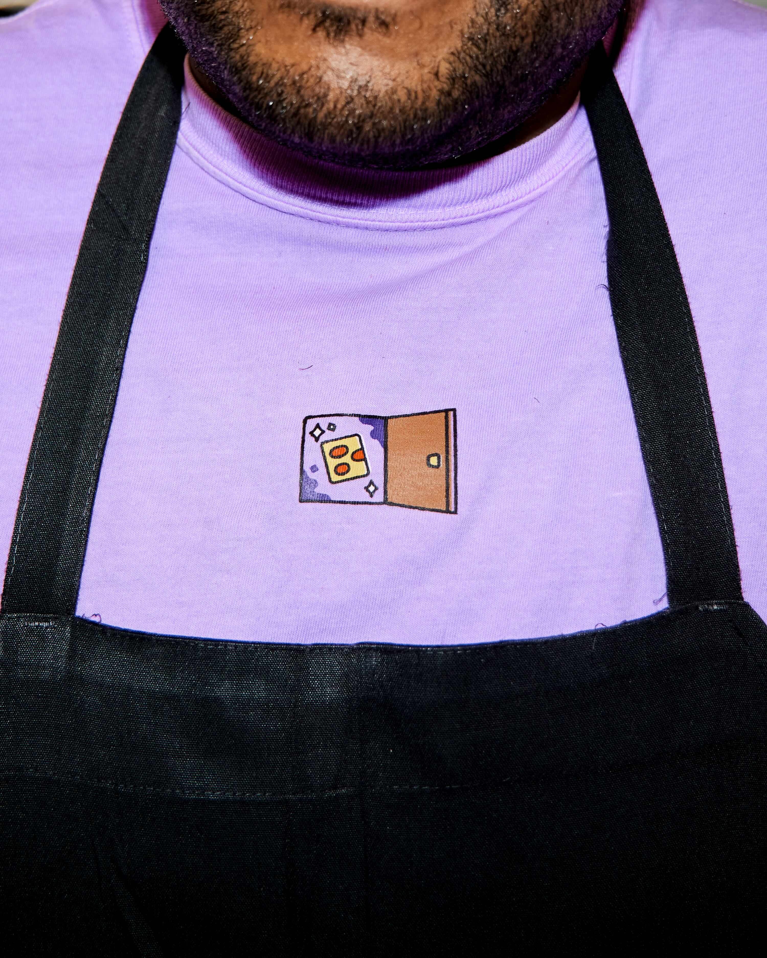 Close-up of a person wearing a light purple t-shirt with an embroidered design and a black apron for Bobbi's Brand Identity.