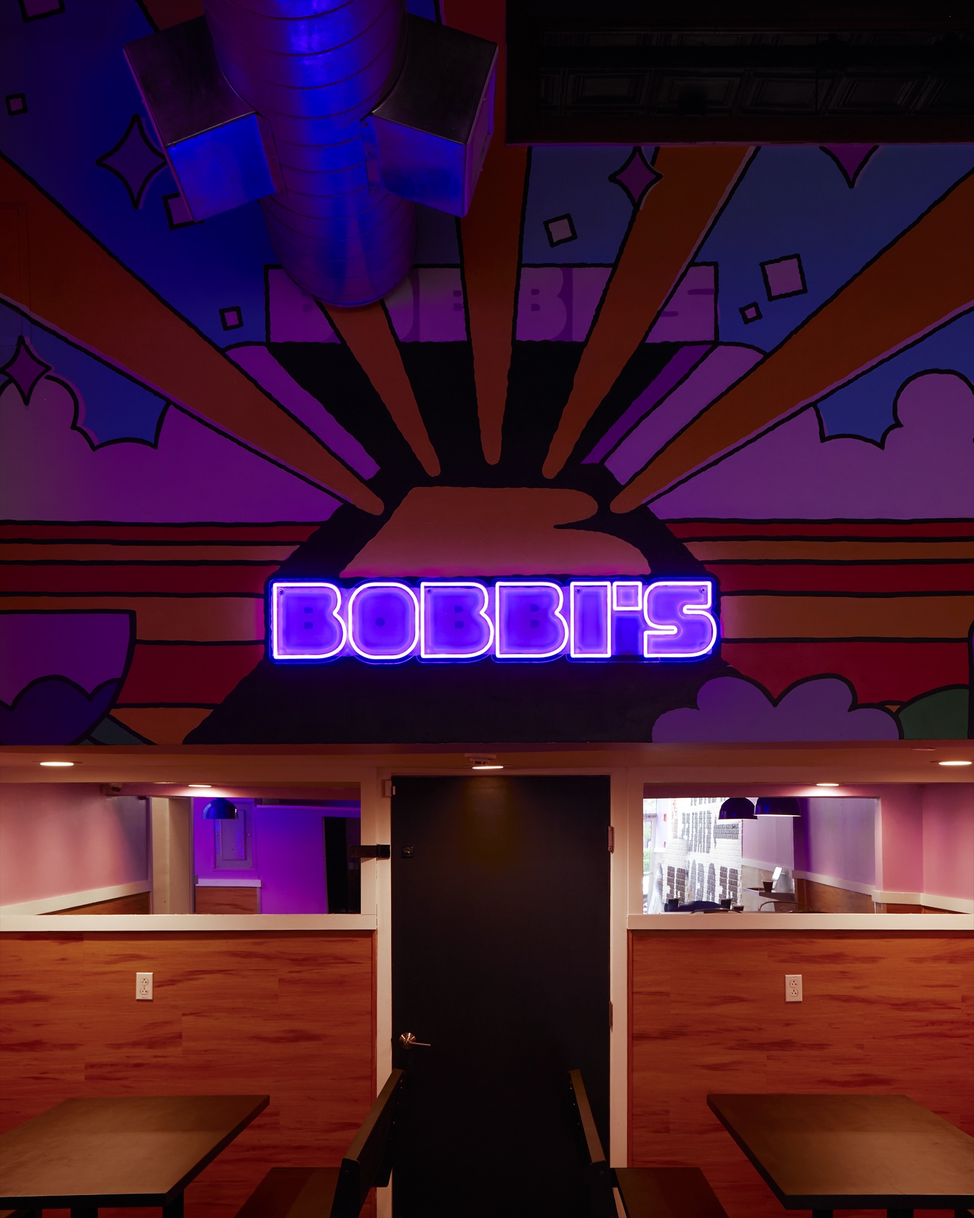 Illuminated purple neon sign displaying Bobbis above a dark central door inside Bobbis restaurant interior