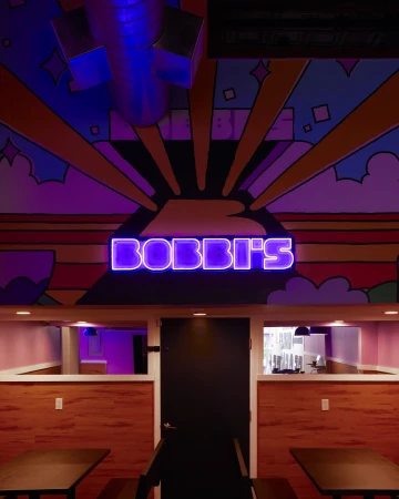 Illuminated purple neon sign displaying Bobbis above a dark central door inside Bobbis restaurant interior