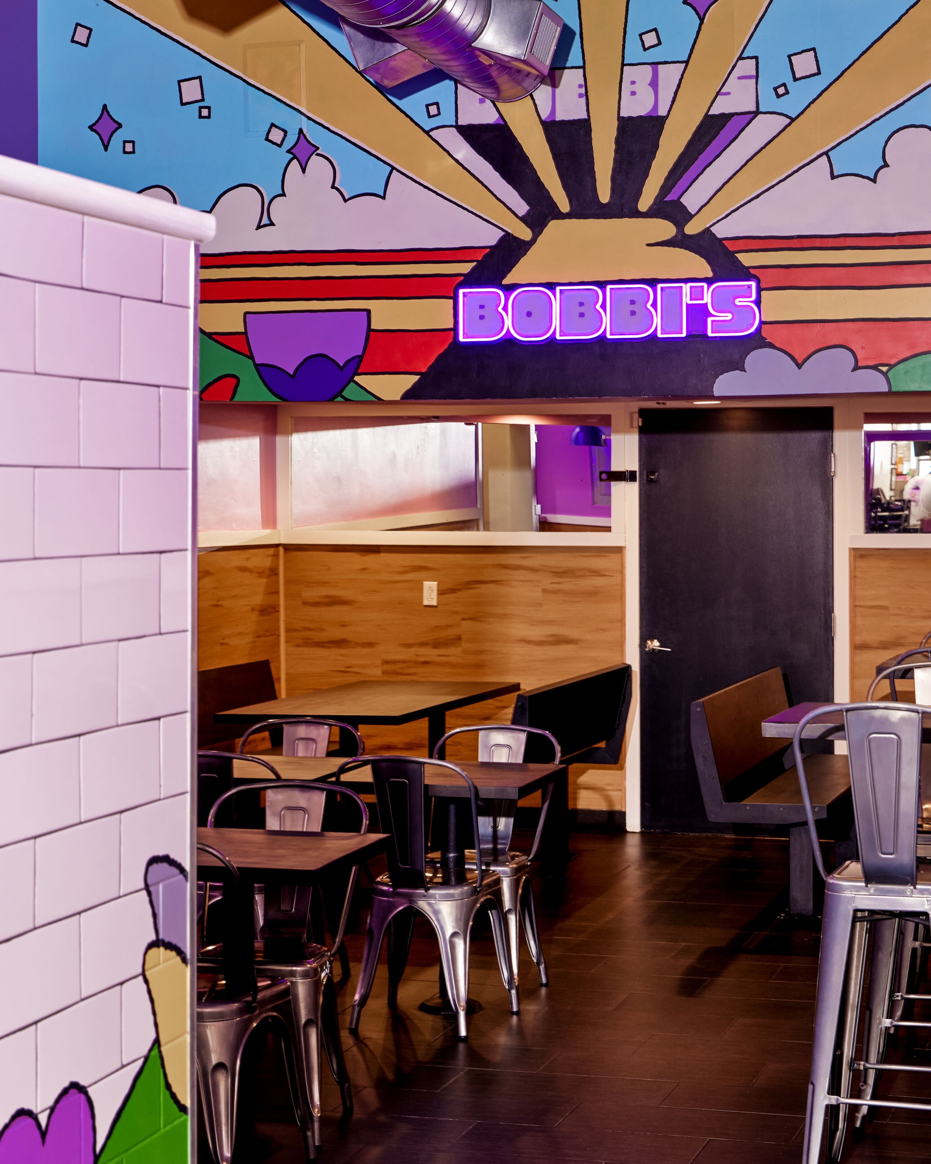 Interior shot of Bobbis restaurant featuring metal chairs, wooden tables, and a colourful painted mural on the upper wall.