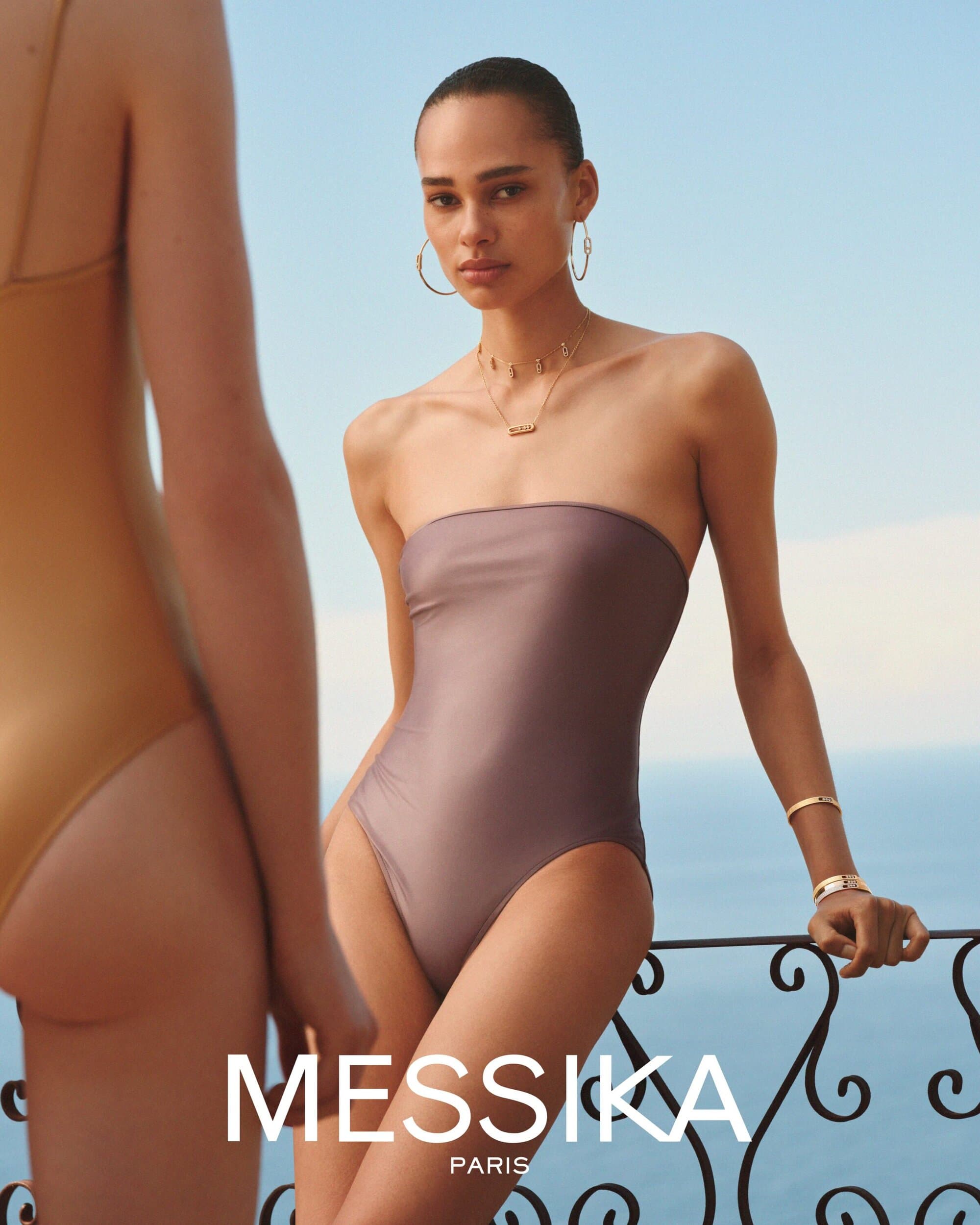 Model wearing jewellery and swimsuit leaning on a balcony railing against an ocean background