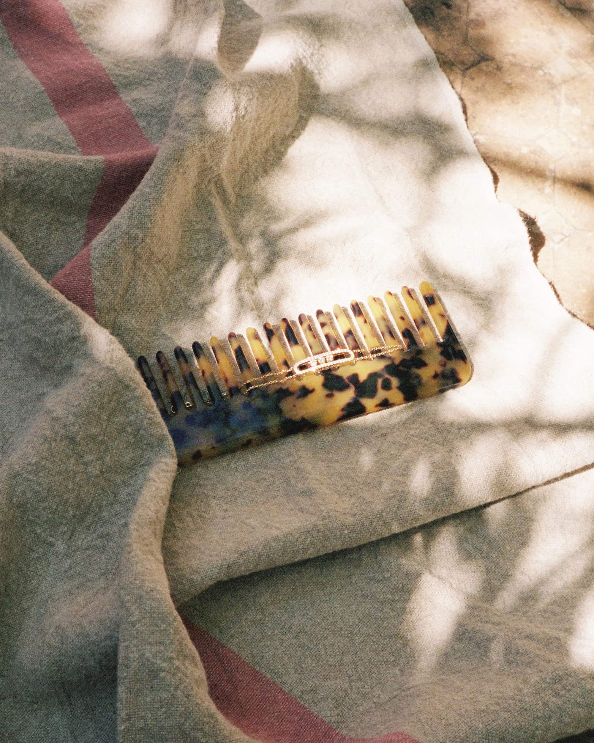 Tortoiseshell hair comb resting on a textured light grey blanket with pink stripes under dappled sunlight.