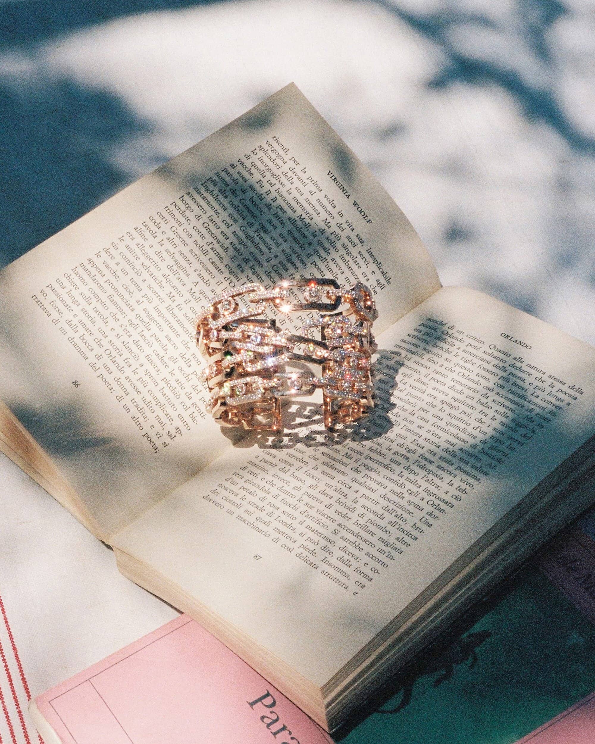 Diamond chain bracelet resting on an open book pages with dappled sunlight under a blue surface