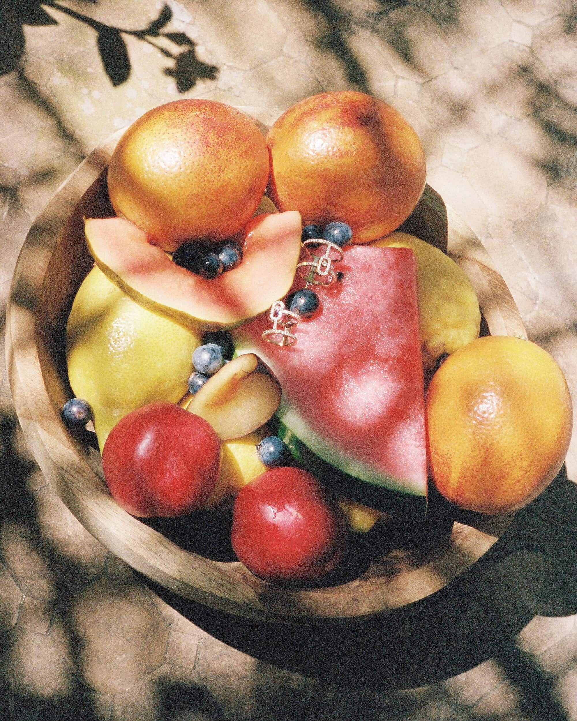 Wooden bowl filled with assorted tropical fruits including watermelon, citrus, and blueberries, shot from above.
